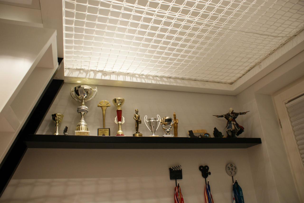 Półka z trofeami, figurkami i medalami pod sufitem z siatki w pokoju.