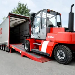 Czerwony wózek widłowy Kalmar na rampie ładunkowej ciężarówki z otwartą naczepą, widoczny operator w kabinie.