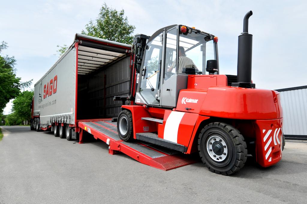 Czerwony wózek widłowy Kalmar na rampie ładunkowej ciężarówki z otwartą naczepą, widoczny operator w kabinie.