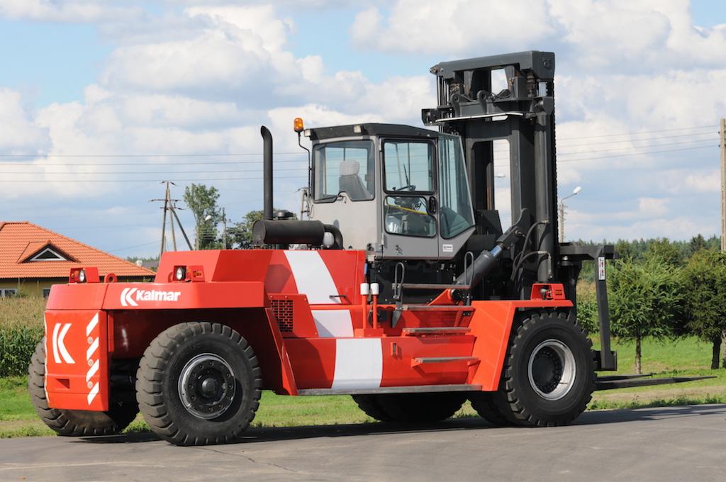 Czerwono-szary wózek widłowy Kalmar z białymi pasami, zaparkowany na betonowym placu, widoczne opony, kabina operatora i maszt podnoszący.