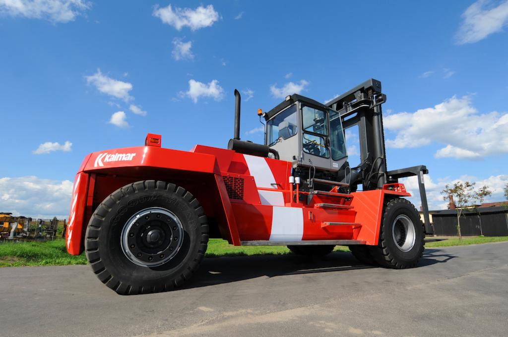 Czerwony wózek widłowy Kalmar z białymi pasami na tle błękitnego nieba z chmurami, stojący na betonowej powierzchni.