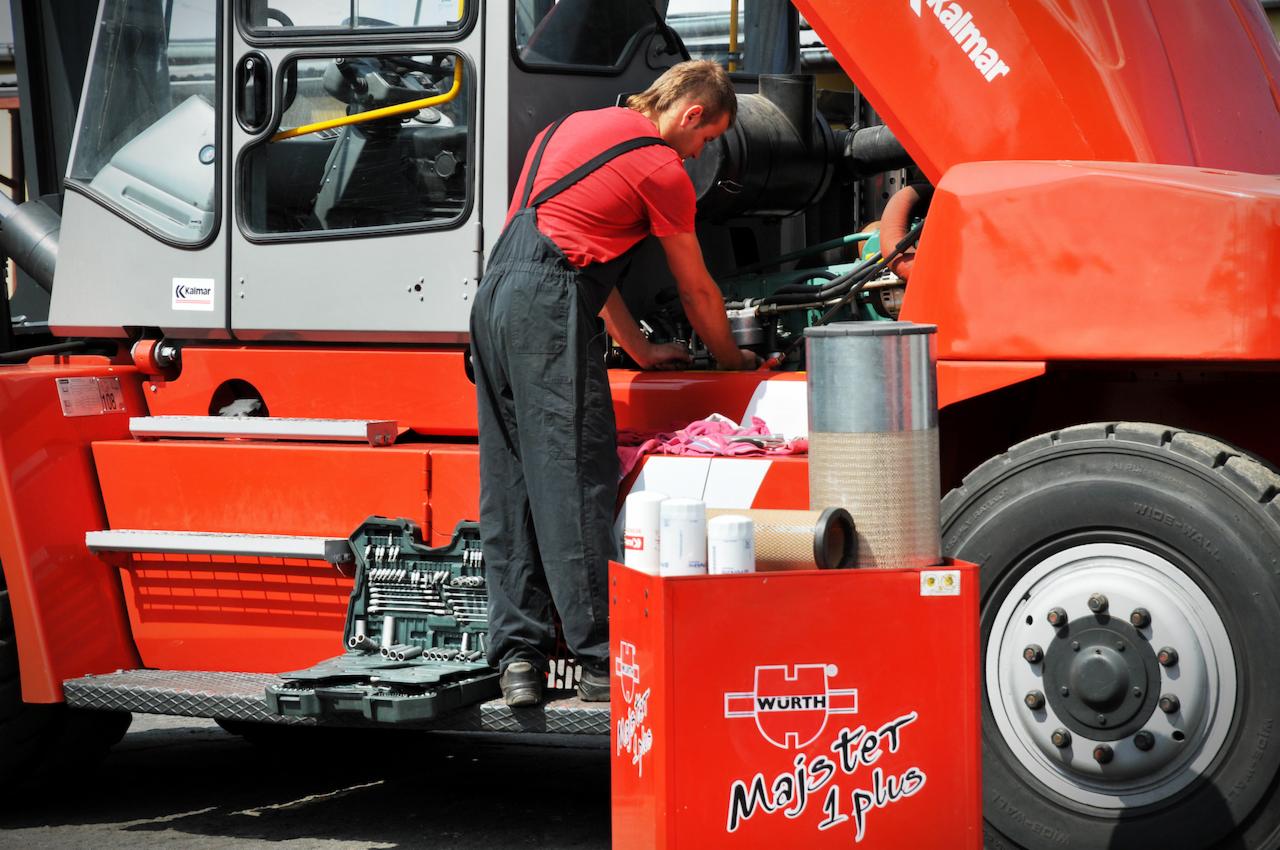 Mechanik w czerwonej koszulce i czarnych ogrodniczkach naprawia silnik pomarańczowego wózka widłowego Kalmar, obok skrzynka narzędziowa Wurth Majster 1 plus i filtry.