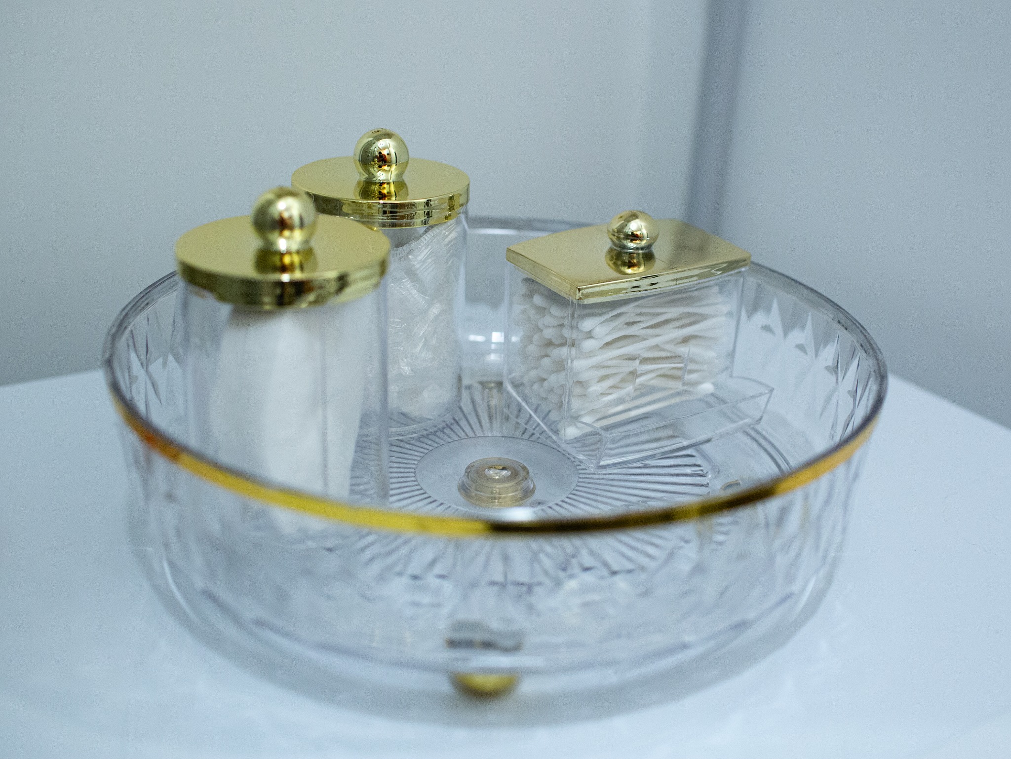 Przezroczysty organizer łazienkowy z trzema pojemnikami na waciki, patyczki kosmetyczne i inne akcesoria, z elementami w kolorze złotym.