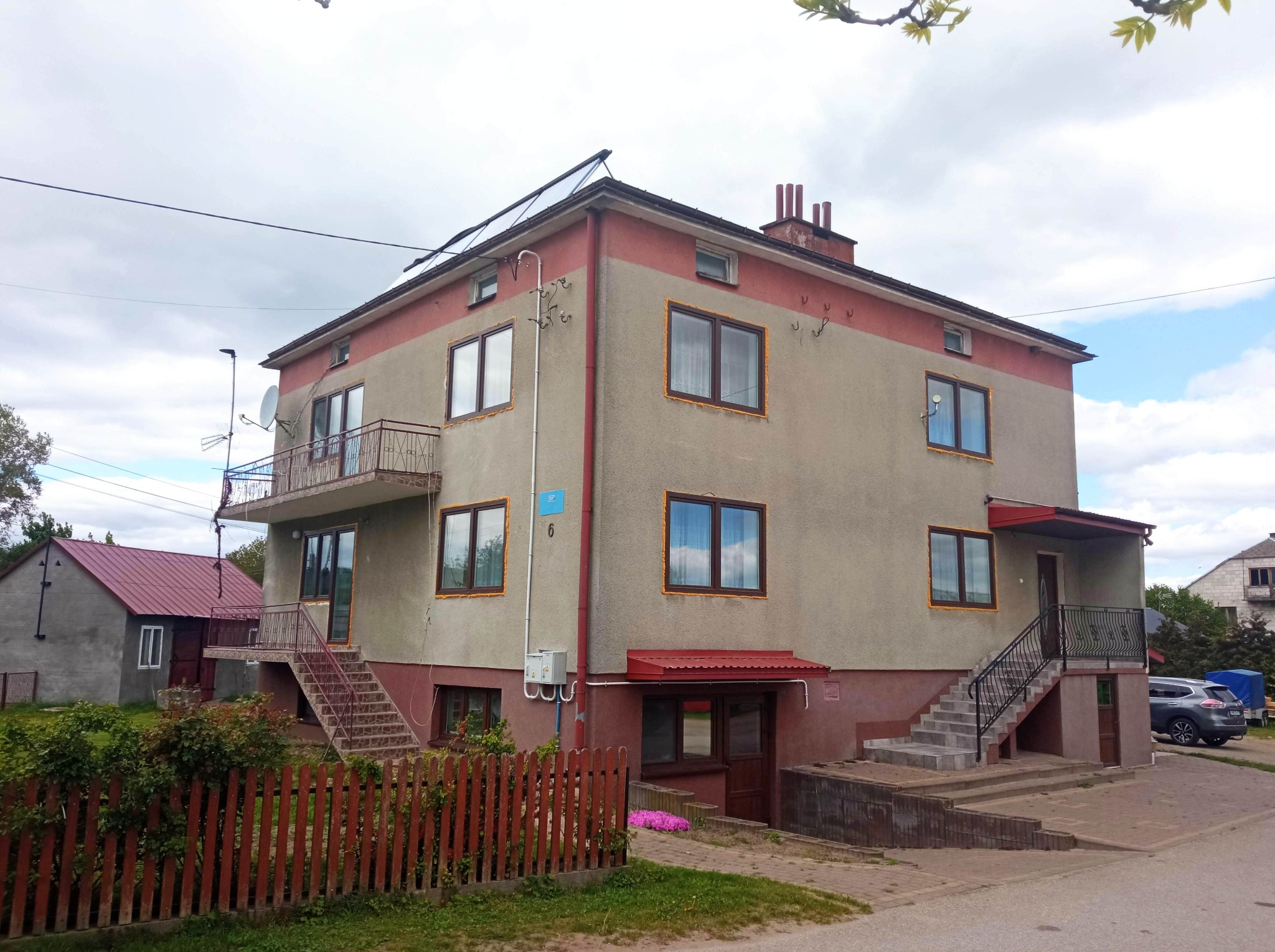Dwupiętrowy dom z oknami PCV, częściowo ocieplony, z panelami słonecznymi na dachu i balkonem z metalową barierką. Widoczne ślady prac termomodernizacyjnych.