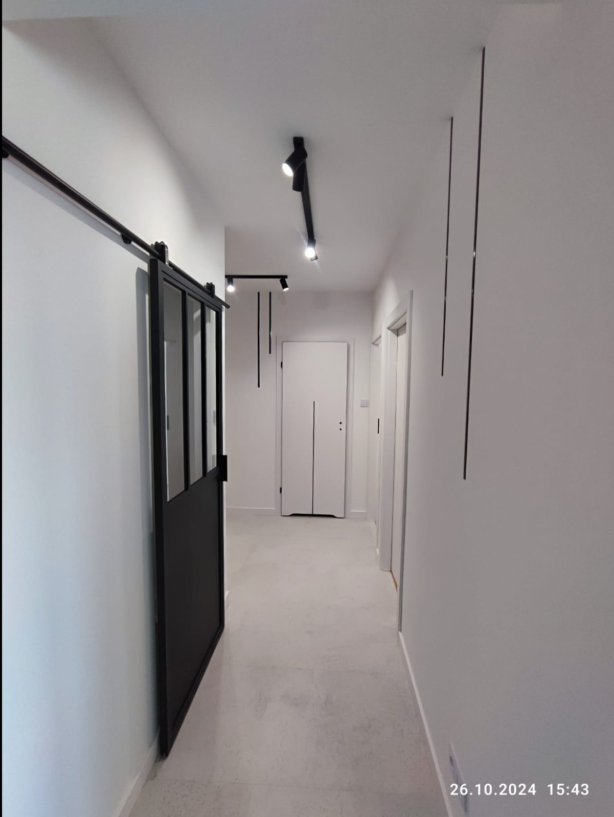 Nowoczesny korytarz z przesuwnymi drzwiami w stylu loft, oświetleniem punktowym i minimalistycznymi dekoracjami ściennymi.