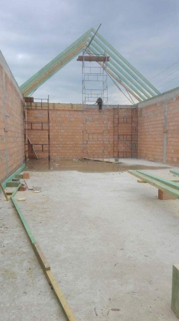 Budowa domu murowanego: widok wnętrza z częściowo wzniesioną więźbą dachową, rusztowaniami i pracownikiem na górze, ściany z cegły, surowy beton na podłodze, drewniane elementy konstrukcyjne...