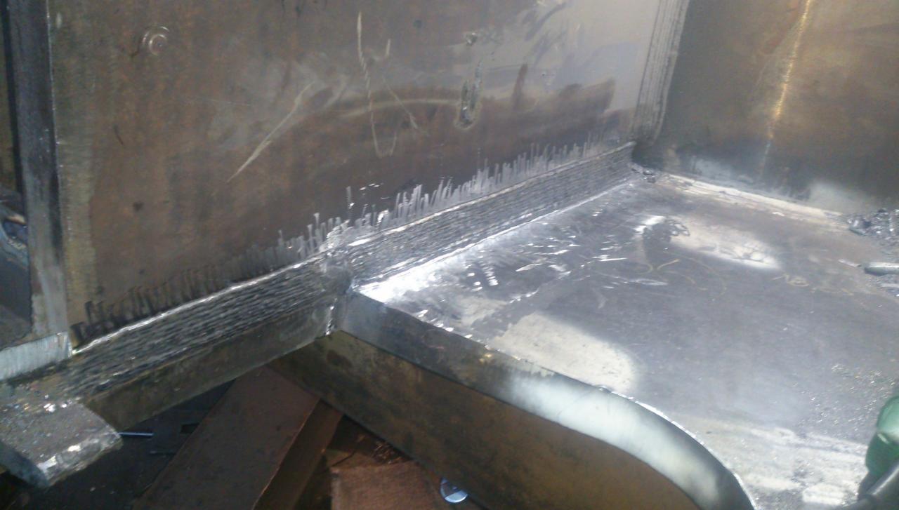 Wnętrze metalowej konstrukcji po spawaniu, widoczne spawy narożne z charakterystycznymi odpryskami i śladami obróbki.