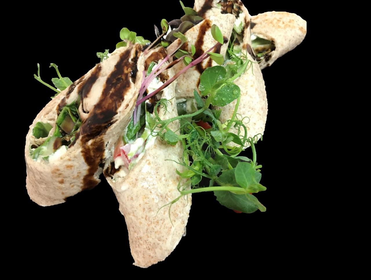 Wrapy z pełnoziarnistej tortilli z kremowym serem, warzywami i sosem balsamicznym, udekorowane świeżymi pędami groszku i mikrolistkami, na czarnym tle.