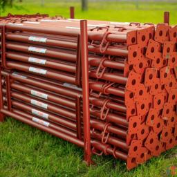 PHU Buildex Krzysztof Puczko - Stos brązowych, metalowych podpór budowlanych z kwadratowymi podstawami, ułożonych na trawie.