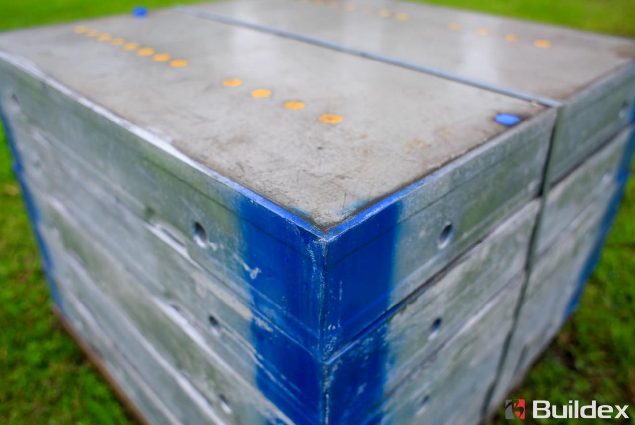 Stos szalunków budowlanych z metalowym obramowaniem pomalowanym na niebiesko, widoczne żółte oznaczenia na powierzchni, ułożone na trawie w Głogowie.