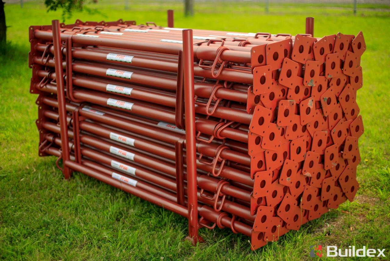 Stos brązowych, metalowych podpór budowlanych z kwadratowymi podstawami, ułożonych na trawie.