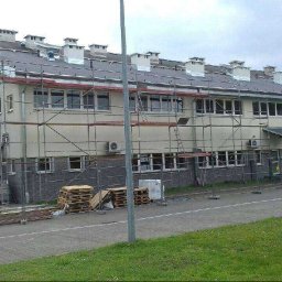 LARIX Janusz Wójcik - Budynek w trakcie remontu dachu; widoczne rusztowania, materiały budowlane i kominy. Szary dach z licznymi kominami.