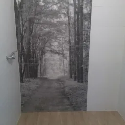 Wykończona łazienka z podłogą imitującą drewno i ścianą pokrytą płytkami z motywem czarno-białego lasu, widoczny odpływ liniowy.