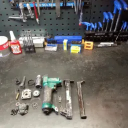 Rozłożony pneumatyczny gwoździarka na warsztatowym stole, widoczne narzędzia, części zamienne i akcesoria do naprawy.