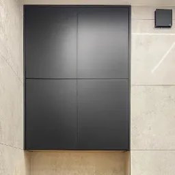 Czarna szafa wnękowa z czterema drzwiami, wbudowana w ścianę z jasnymi płytkami i trójkątnym oświetleniem LED, minimalistyczny design.