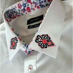 Biała koszula z haftowanymi motywami ludowymi na kołnierzyku i wewnętrznej stronie kołnierza w drobny kwiatowy wzór.