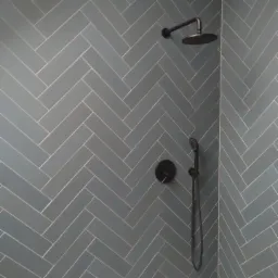 Ściana kabiny prysznicowej wyłożona niebiesko-szarą glazurą w jodełkę z czarną armaturą w Cieszynie.