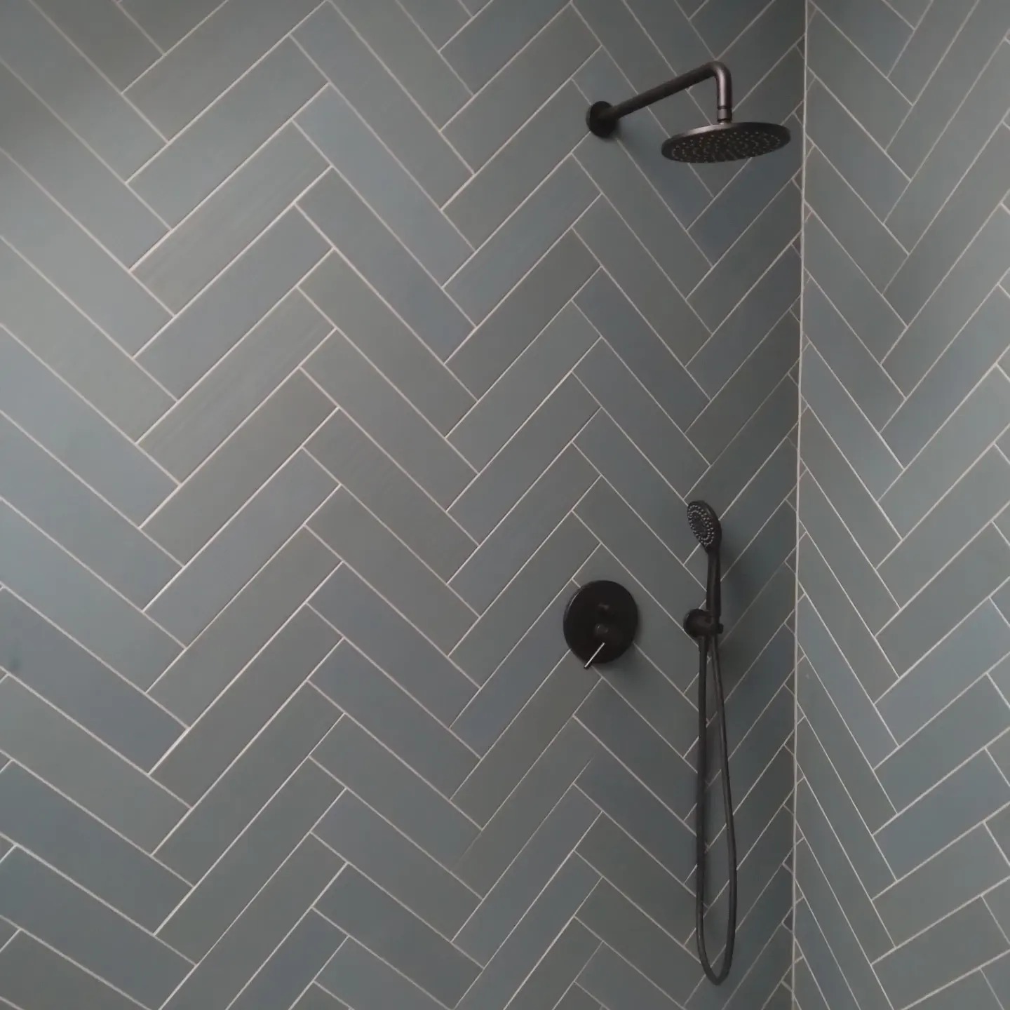 Ściana kabiny prysznicowej wyłożona niebiesko-szarą glazurą w jodełkę z czarną armaturą w Cieszynie.