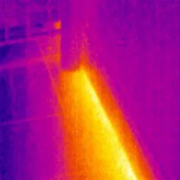 Termogram okna ukazujący ucieczkę ciepła w postaci żółto-pomarańczowej smugi na fioletowym tle ściany.
