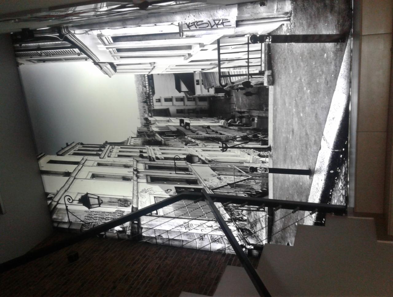 Sufit napinany z nadrukiem czarno-białej fotografii miejskiej, widoczna część schodów i ściany.