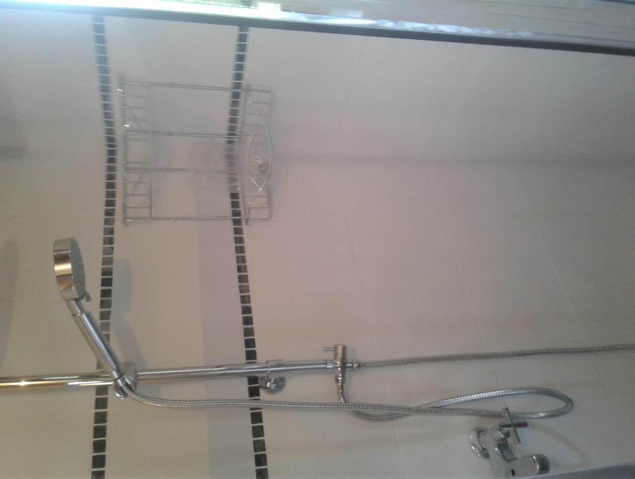 Zamontowany chromowany zestaw prysznicowy z półką na akcesoria w wykafelkowanej łazience, widok z dołu.