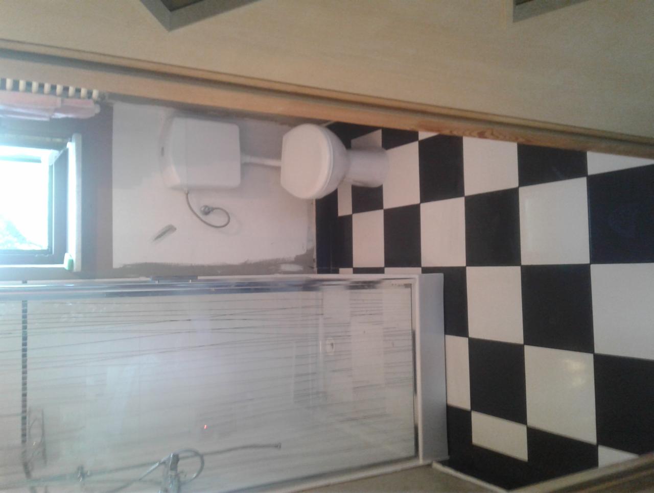 Ukończona łazienka z kabiną prysznicową i toaletą, wykończona biało-czarnymi płytkami w szachownicę, widoczne ślady po niedawnych pracach wykończeniowych.