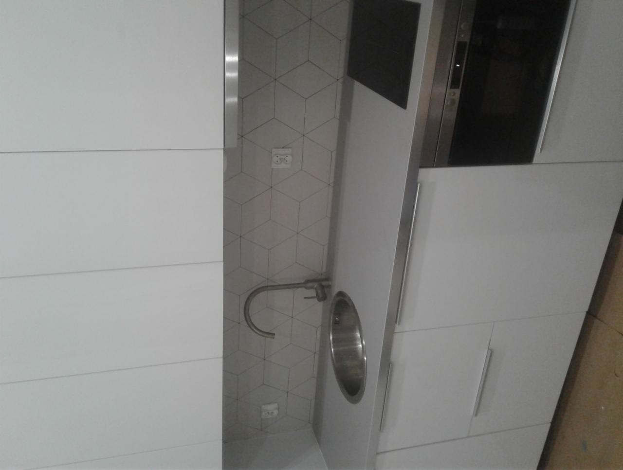 Nowoczesna łazienka z białą zabudową, umywalką wpuszczaną w blat i geometryczną mozaiką na ścianie.