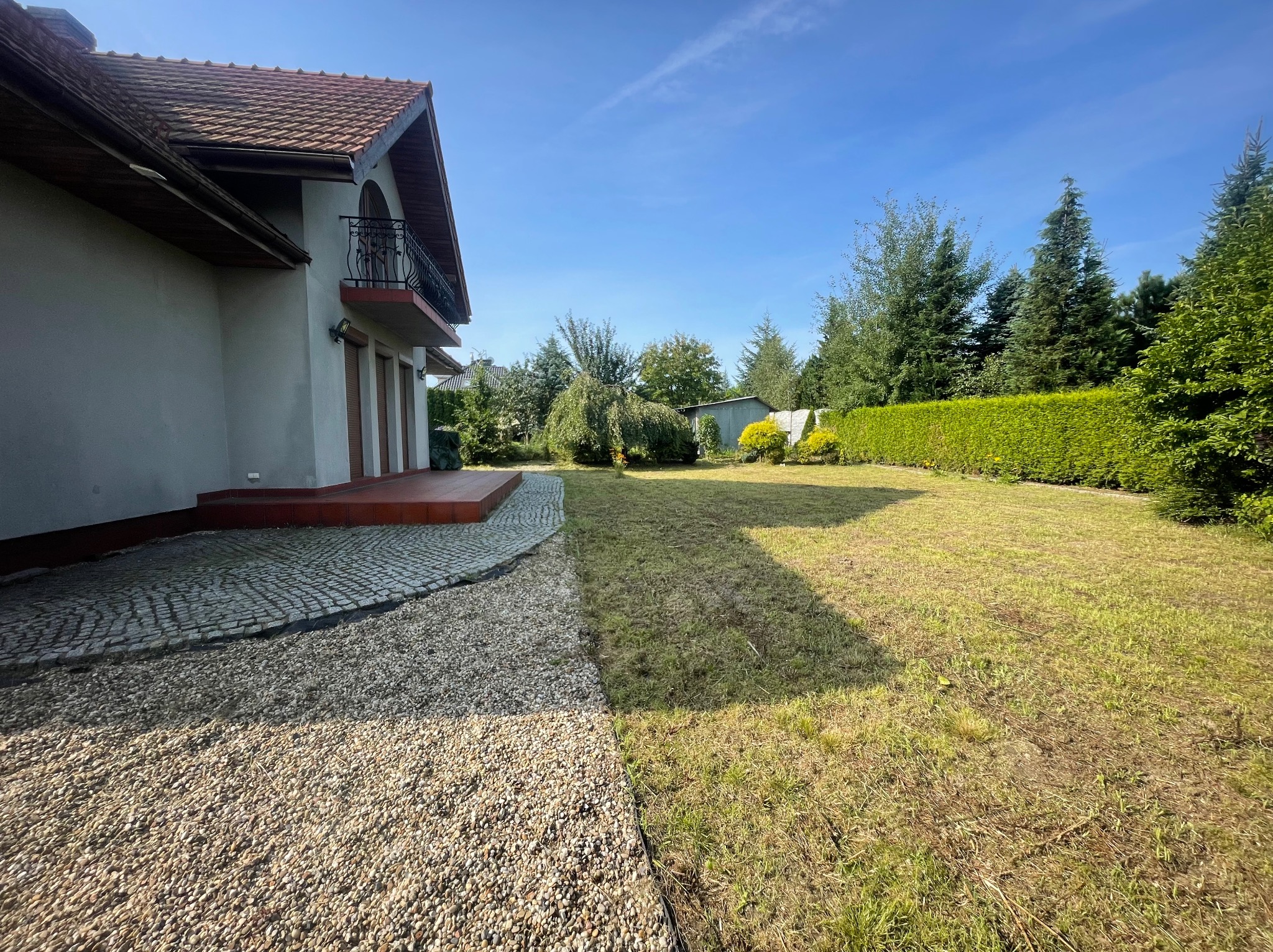 Widok na ogród z kostką brukową i kamieniami ozdobnymi w Gorzycach. W tle dom z balkonem i zadbany trawnik.