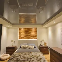 Nowoczesna sypialnia z drewnianą dekoracją ścienną i błyszczącym, podwieszanym sufitem, odbijającym elementy wystroju, uzupełniona obrazem koni i minimalistycznymi lampkami nocnymi.