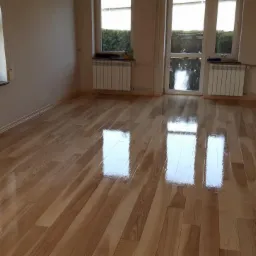Błyszcząca, świeżo polakierowana podłoga z jasnego drewna w pustym pokoju z oknami i grzejnikami.