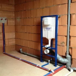 Stelaż podtynkowy Grohe zamontowany na tle surowej ściany z cegły, widoczne rury instalacji wodnej i kanalizacyjnej w trakcie montażu.