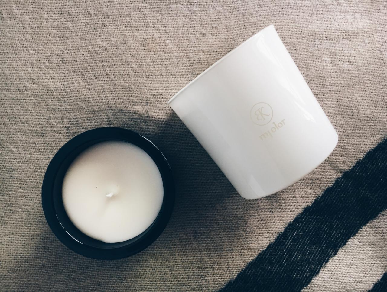 Dwie świece w minimalistycznych pojemnikach: czarny i biały, na tle lnianej tkaniny z ciemnym pasem.