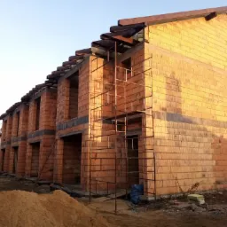 Wznoszenie ścian z pustaków ceramicznych na budowie szeregowca, widoczne rusztowania i przygotowany piasek.