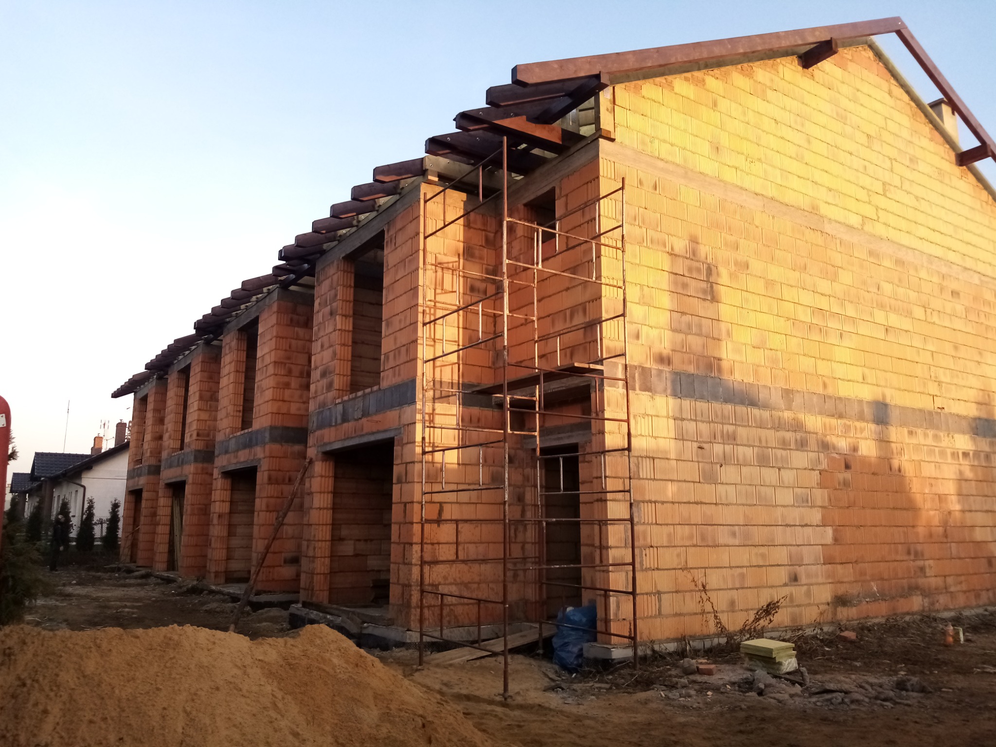 Wznoszenie ścian z pustaków ceramicznych na budowie szeregowca, widoczne rusztowania i przygotowany piasek.