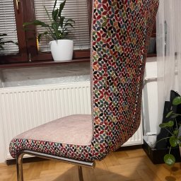 FIRMA FASTRYGA Lubow Jankowicz - Krzesło po renowacji z nową tapicerką w kolorowy wzór, na metalowych nogach. W tle okno z żaluzjami i roślina doniczkowa. Widok z boku, na podłodze parkiet.
