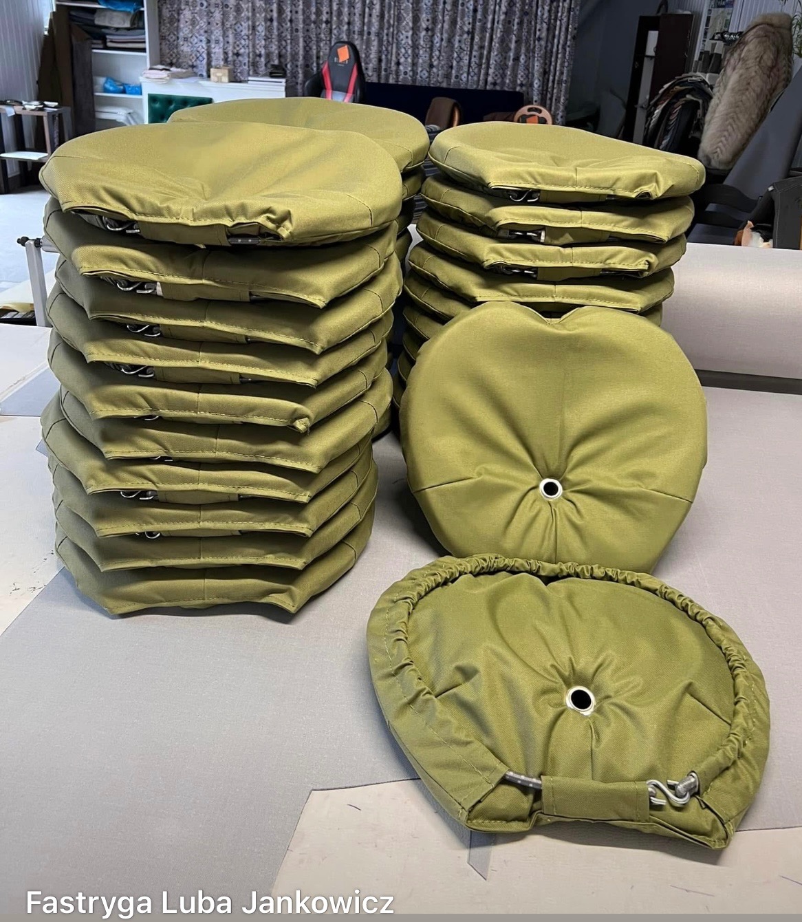 Stosy oliwkowych pokrowców na krzesła/poduszki z otworem na środku, wykonane z gładkiej tkaniny. Widoczne detale mocowań i sznurków ściągających.