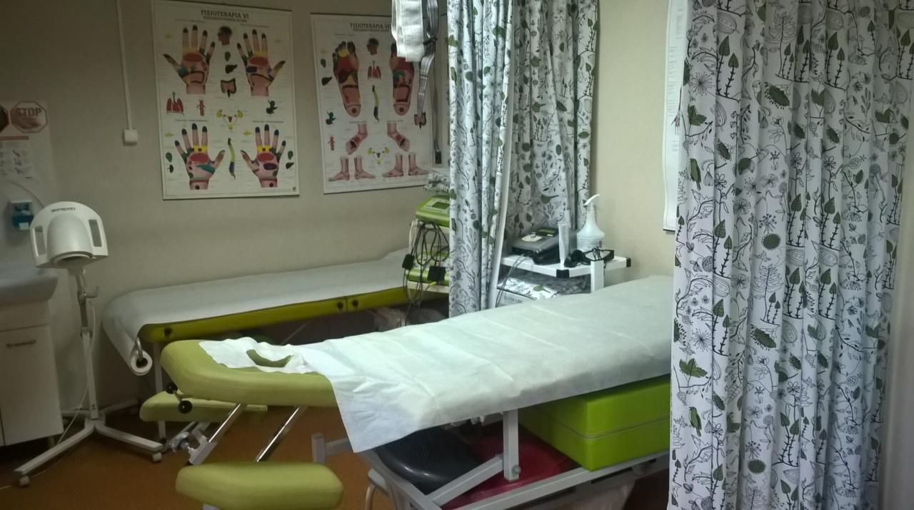 Gabinet z dwoma leżankami przykrytymi białym papierem, na ścianach plakaty z mapami punktów na dłoniach i stopach, zasłona z motywem roślinnym.