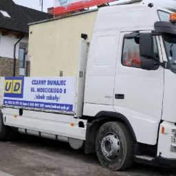 Biała ciężarówka Volvo z dźwigiem HIAB i reklamą składu budowlanego KAL-BUD na tle budynku z elementami kamiennymi.