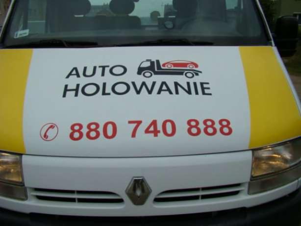 Przód białego samochodu lawety z żółtymi pasami i czarno-czerwonym napisem 'AUTO HOLOWANIE 880 740 888' oraz grafiką lawety z samochodem na górze.