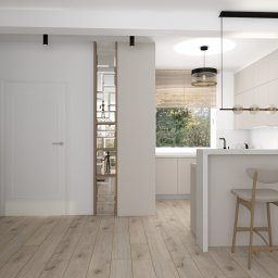 B-projekt - Jasne wnętrze mieszkania z drewnianą podłogą, szafką z okrągłym wzorem, lustrem w ozdobnej ramie, ścianką działową z lustrami i widokiem na kuchnię z hokerami.