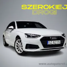 Białe Audi A4 na szarym tle z tekstem 'Szerokiej drogi' i adresem strony internetowej na dole.