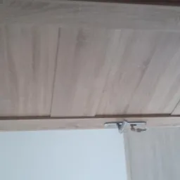 Fragment drewnianych drzwi wewnętrznych w odcieniach jasnego drewna, z widocznym zamkiem i kluczem, sfotografowane pod kątem.