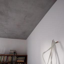 DSX sp. z.o.o - Wykończony sufit z efektem betonu architektonicznego, widoczne wystające kable ze ściany i regał z książkami w tle.