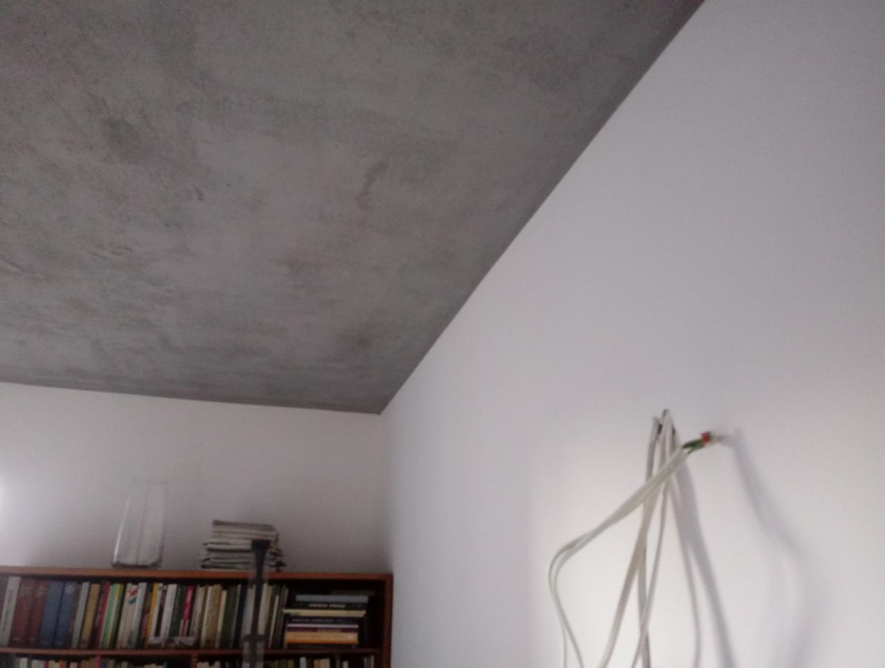 Wykończony sufit z efektem betonu architektonicznego, widoczne wystające kable ze ściany i regał z książkami w tle.