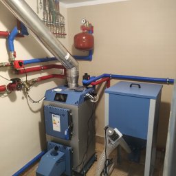 P.H.U. ANTA ZDZISŁAW PRZYGODZKI - Kotłownia z kotłem na pellet PellPal 12, zasobnikiem, rurami instalacji CO i grzejnikami w tle, widoczne elementy instalacji hydraulicznej.