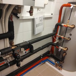 P.H.U. ANTA ZDZISŁAW PRZYGODZKI - Instalacja kotłowni z szarym zasobnikiem ciepłej wody, rurami w izolacji termicznej, zaworami kulowymi z czerwonymi rączkami oraz dokumentacją techniczną w folii ochronnej.