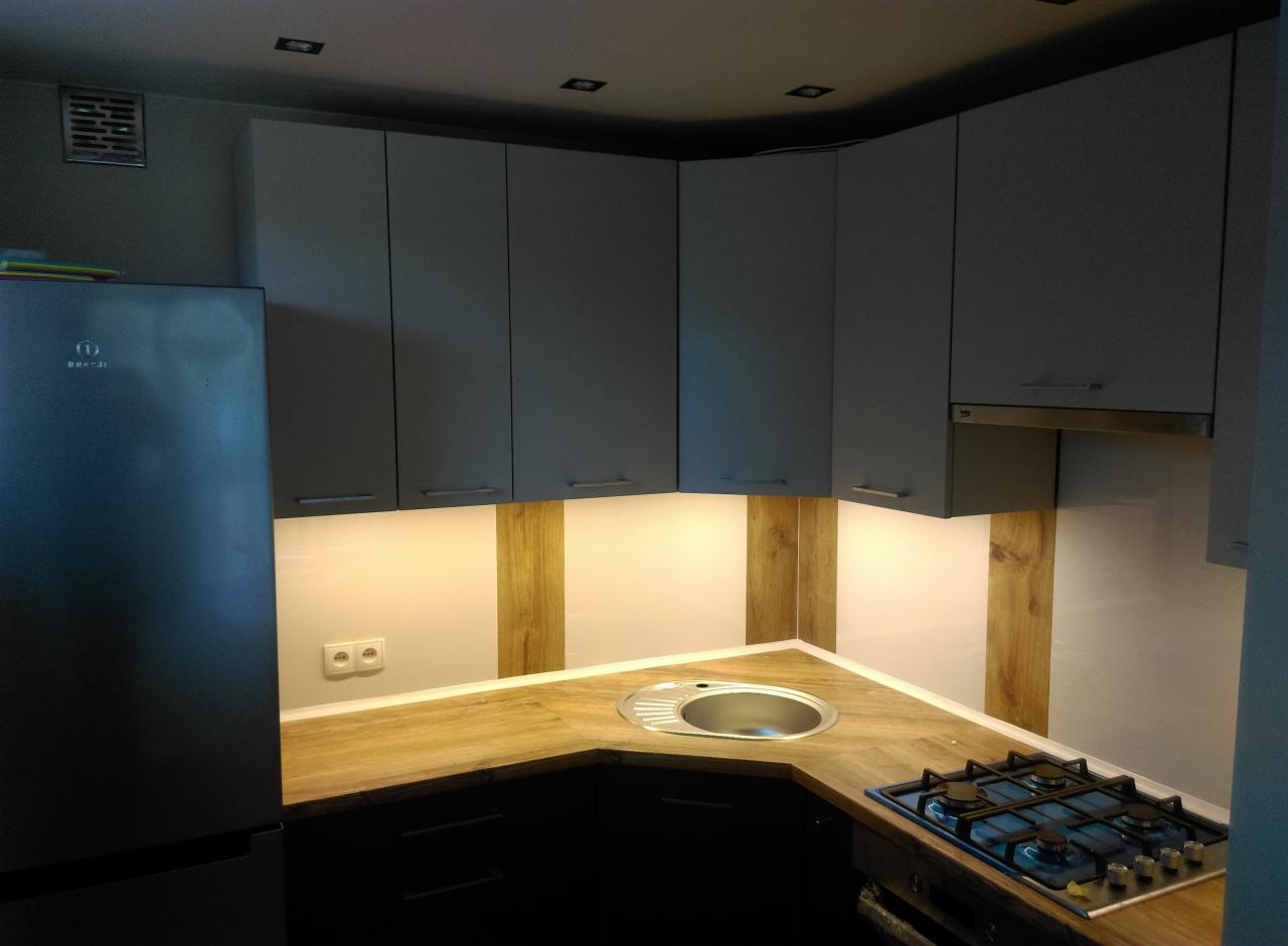 Szara kuchnia na wymiar z drewnianym blatem, oświetleniem podszafkowym i zabudowaną płytą gazową.