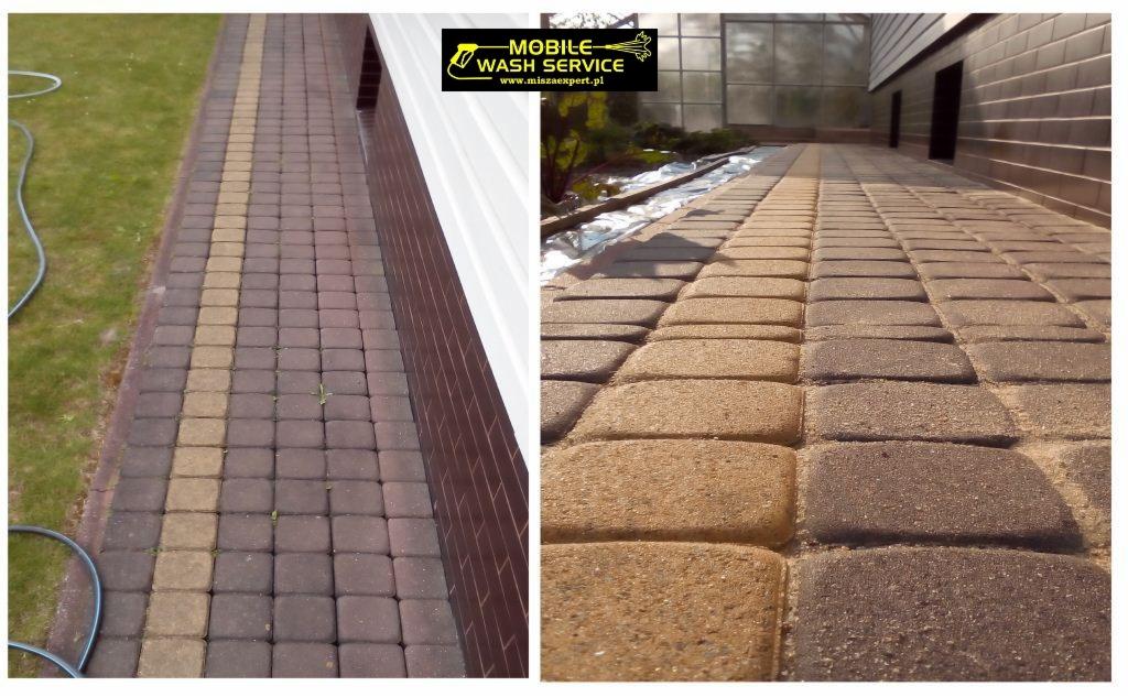 Fragment chodnika z kostki brukowej, z widoczną różnicą w czystości po lewej stronie, gdzie kostka jest ciemniejsza i brudna, oraz po prawej, gdzie kostka jest jaśniejsza i czysta; w tle budynek...