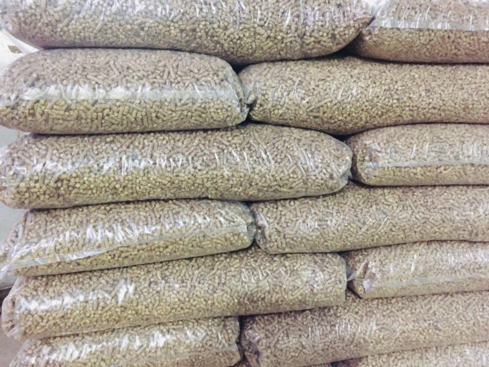 Stos worków z pelletem drzewnym, przezroczyste opakowania, lekko rozmyte tło.