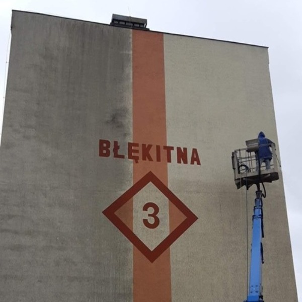 Mycie elewacji budynku z napisem 'Błękitna 3' w Gdyni. Widoczna różnica w czystości ściany po lewej stronie. Pracownik na podnośniku koszowym.